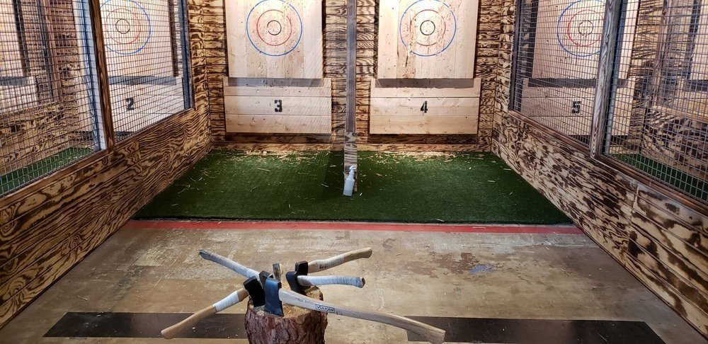 Two painted targets on the burnt wood wall at AXT, each with a bullseye and rings, above the turf and the stump where the axes rest between throws. Source: a guest's photo on the venue's public Yelp listing.